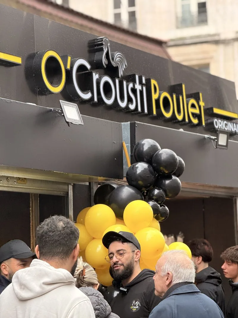 Un franchis&eacute; O'Crousti Poulet en tenue de la marque devant son restaurant le jour de l'ouverture